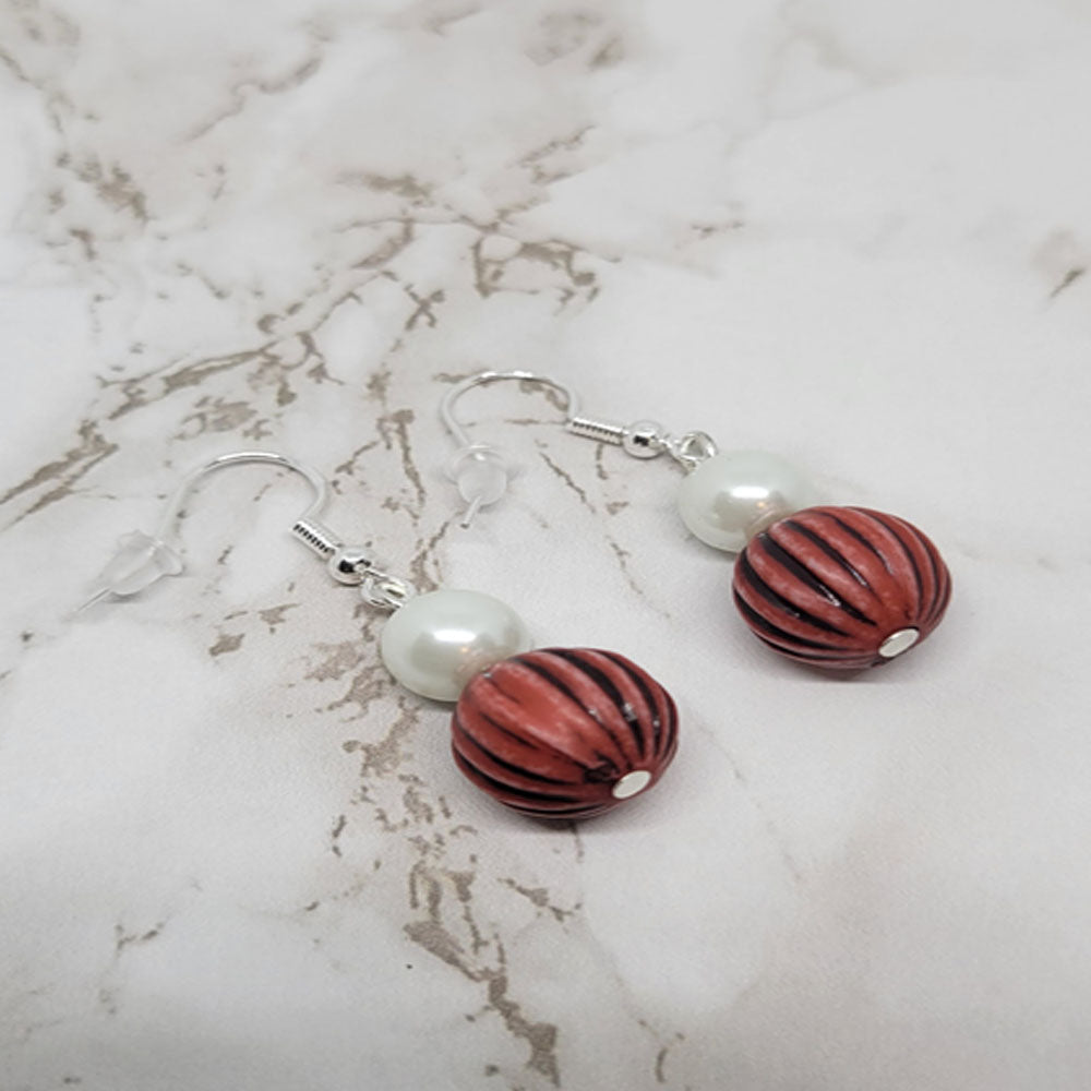 A pair of beaded dangle earrings with red and white pearls, featuring a brown bead at the bottom, on a marble surface.