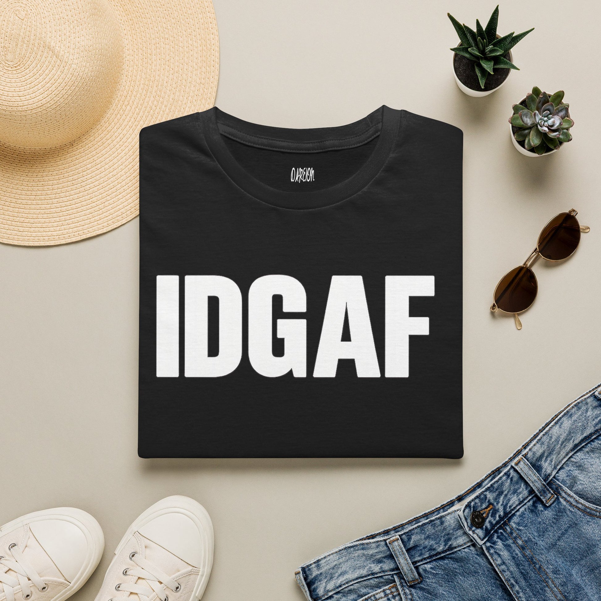 Black t-shirt with 'IDGAF' text on a light surface with casual items like a hat, sunglasses, and jeans.