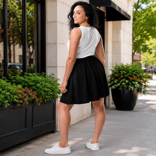 Woman in a white top and black skirt standing on a sidewalk with plants and a building in the background.