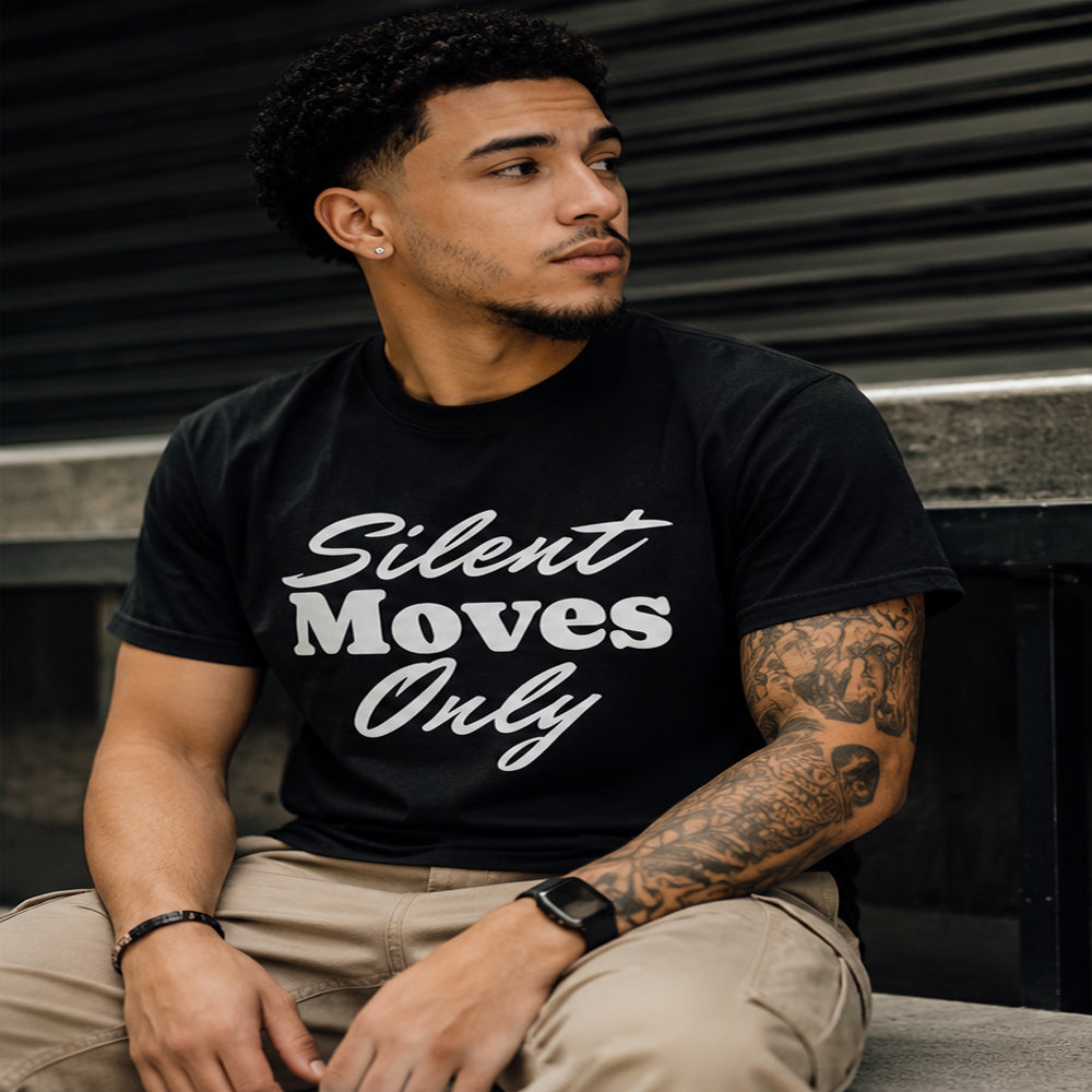 Man wearing a black t-shirt with 'Silent Moves Only' text, sitting against a dark background.