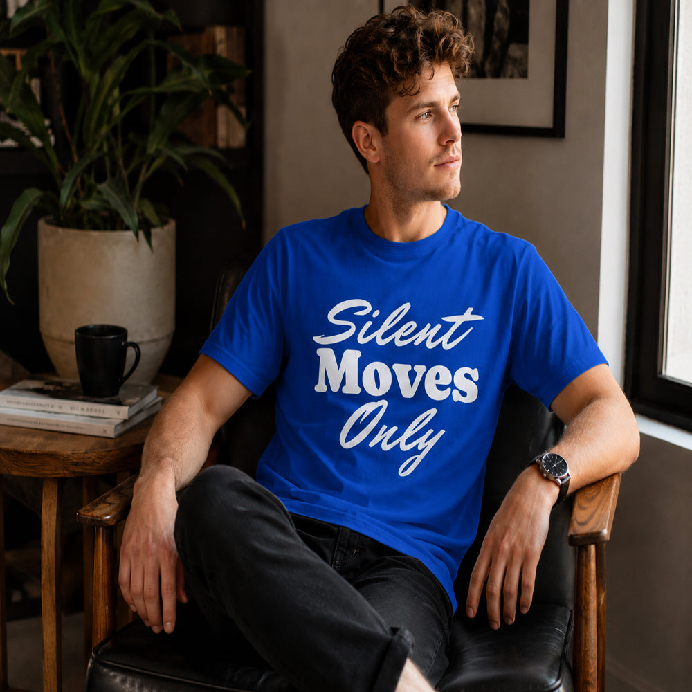 Man wearing a blue t-shirt with 'Silent Moves Only' text, sitting in a room with a plant and books.