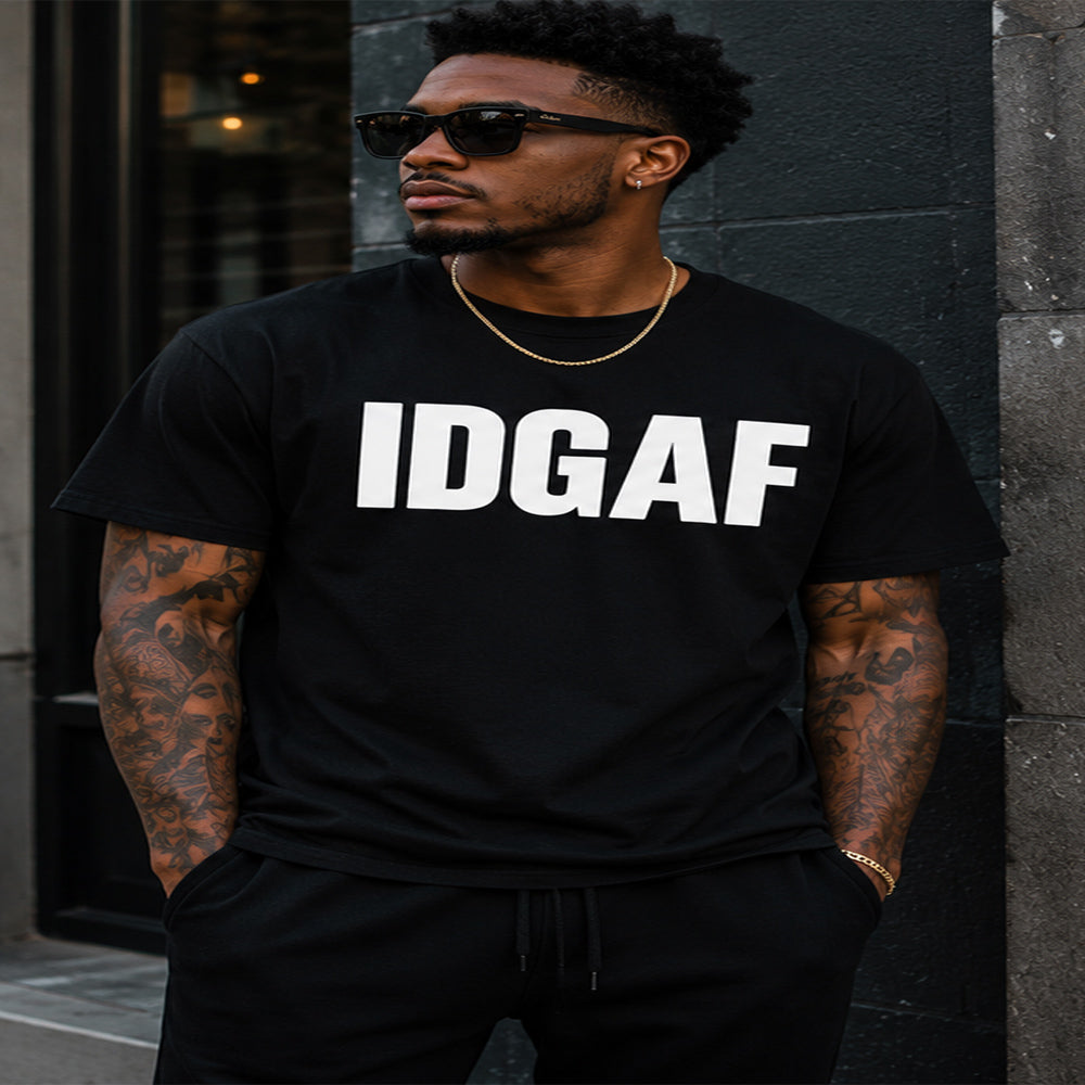 Man wearing a black t-shirt with 'IDGAF' text, standing against a dark wall.