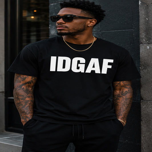 Man wearing a black t-shirt with 'IDGAF' text, standing against a dark wall.