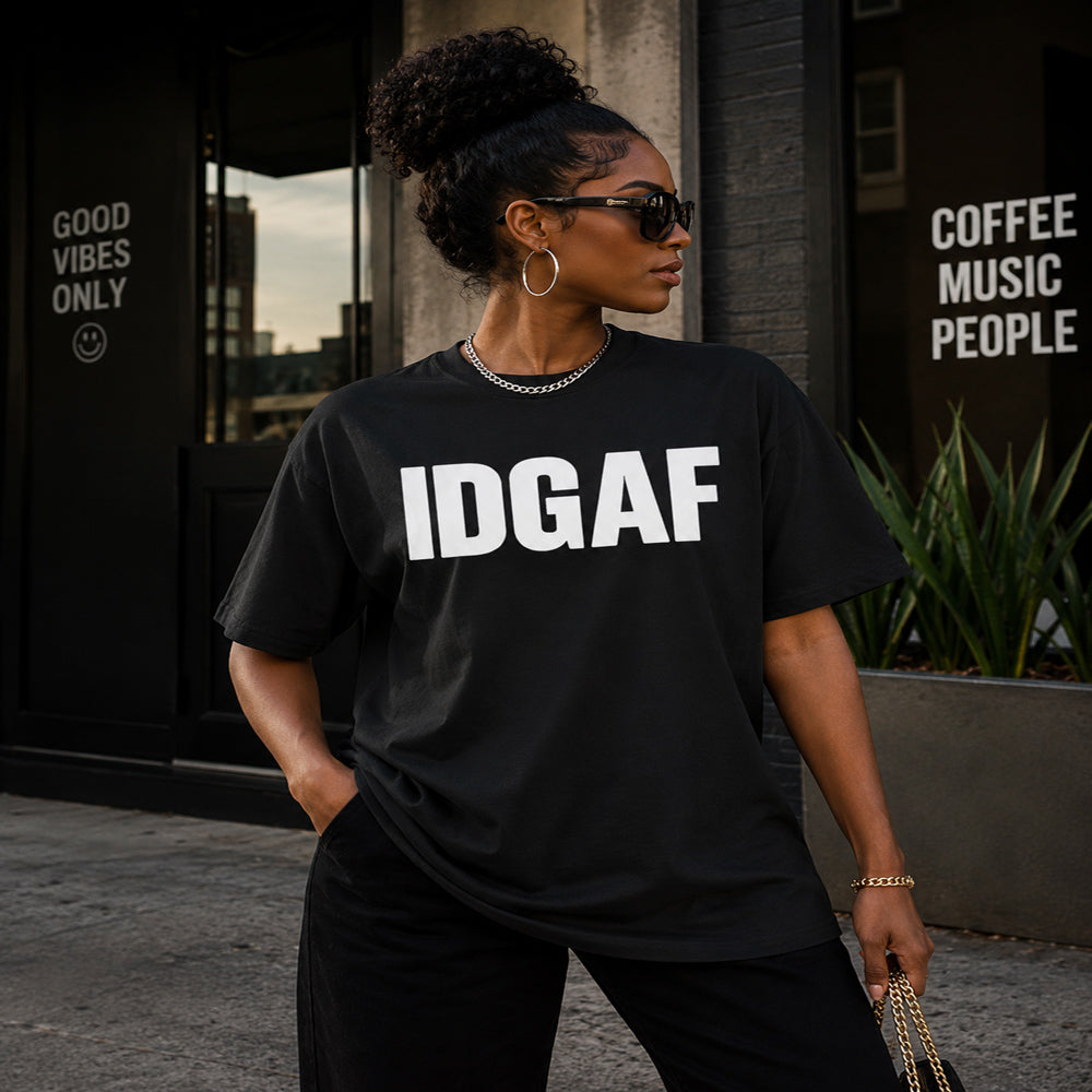 Woman wearing a black t-shirt with 'IDGAF' text, standing in an urban setting.
