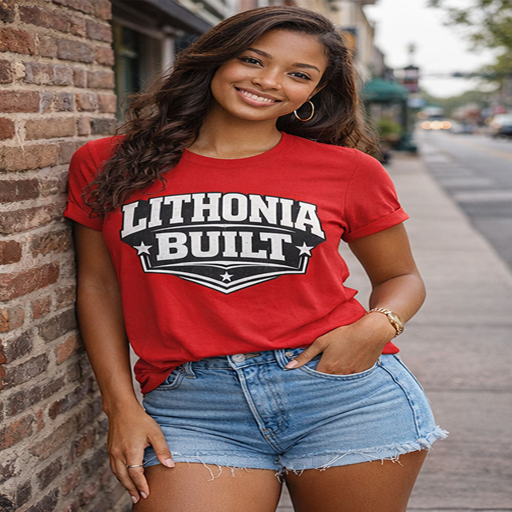 Woman wearing a red 'Lithonia Built' t-shirt standing against a brick wall.