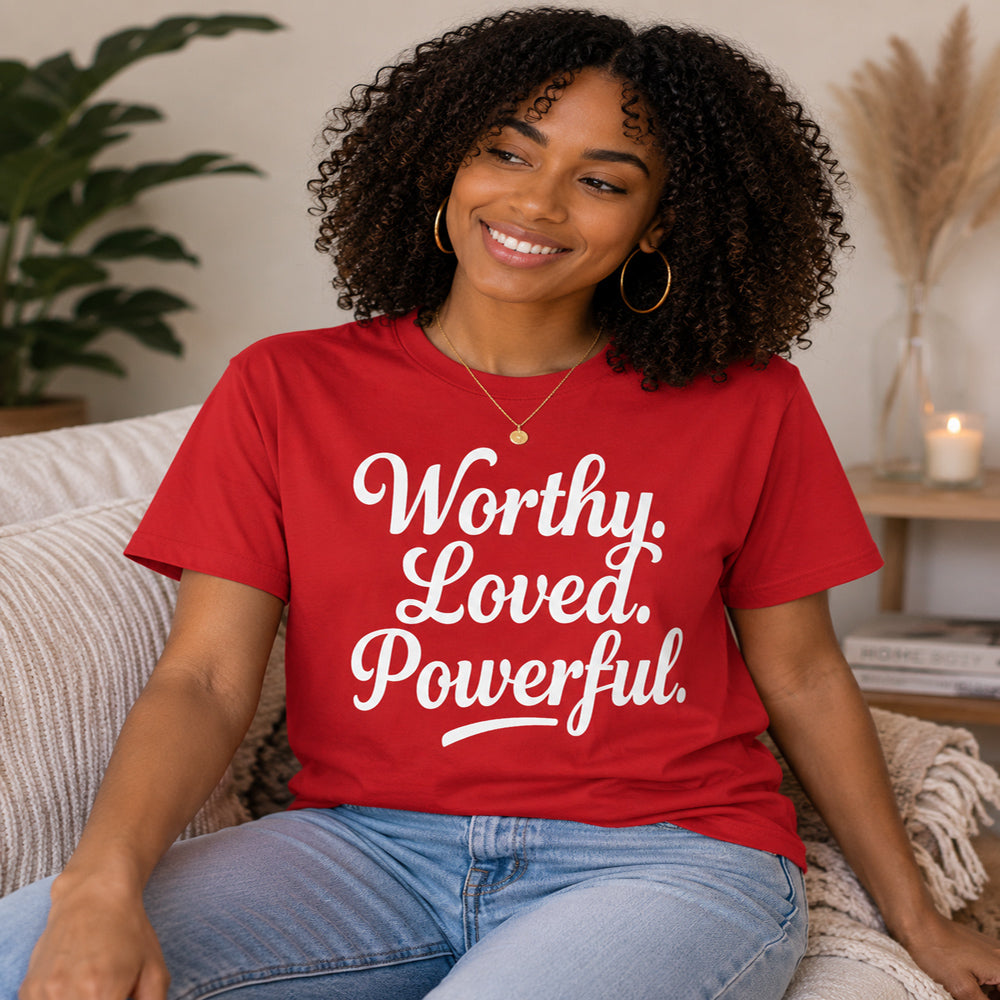 Woman wearing a red t-shirt with 'Worthy. Loved. Powerful.' text, sitting on a couch.