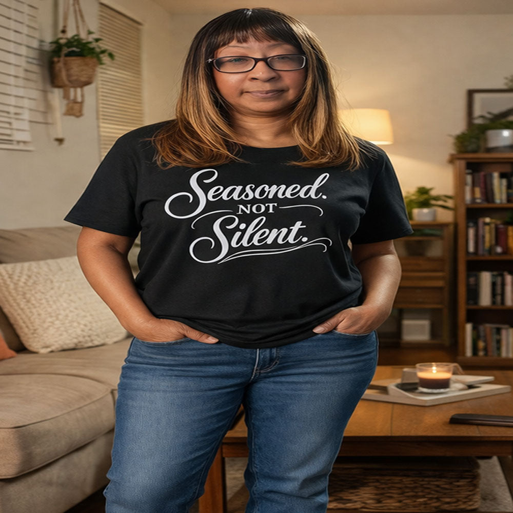 Woman wearing a black t-shirt with 'Seasoned, Not Silent' text in a living room.