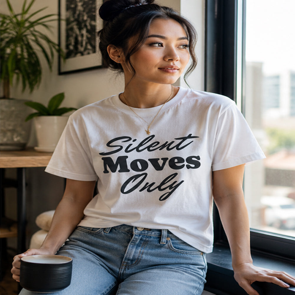 Woman wearing a white t-shirt with 'Silent Moves Only' text, sitting by a window.