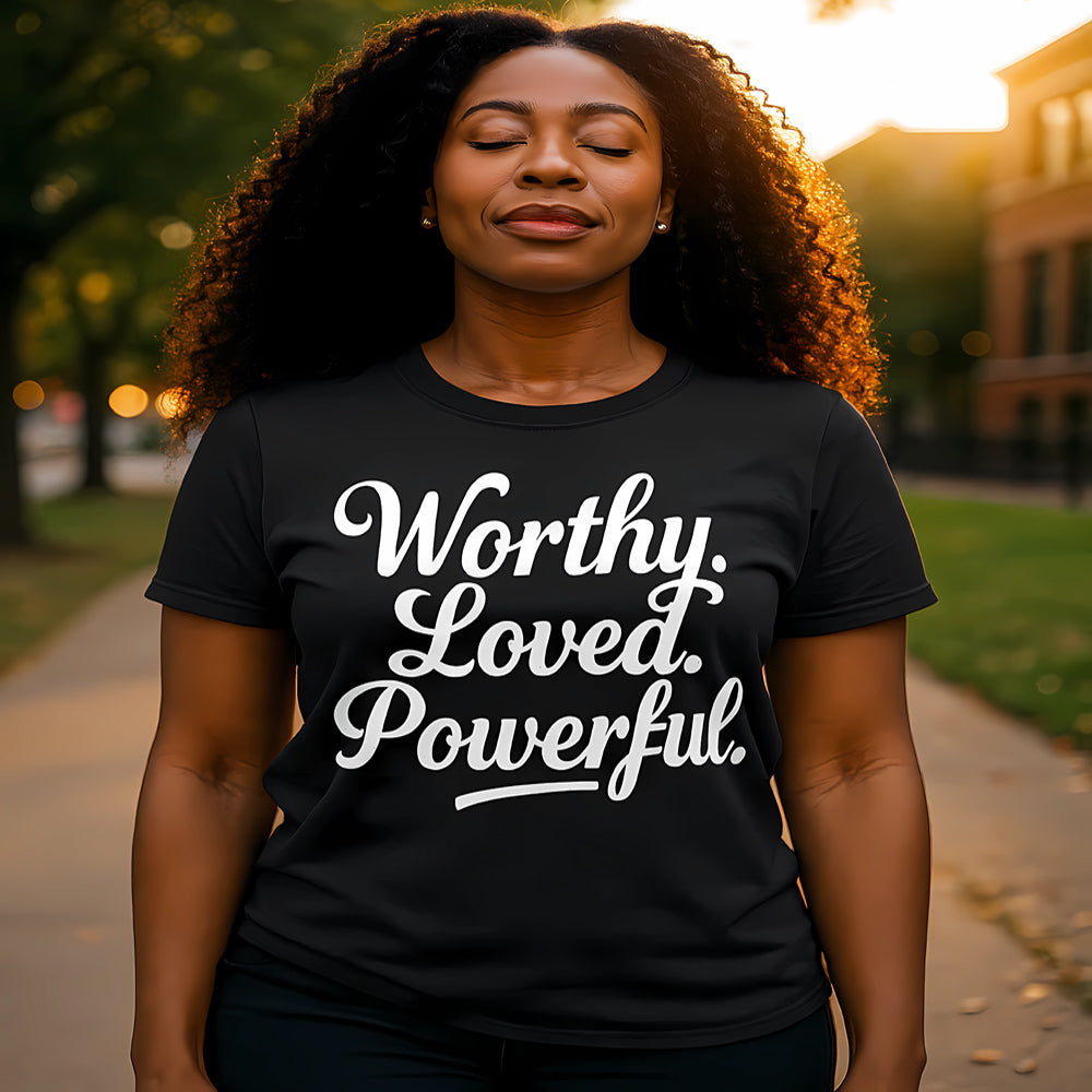 Woman wearing a black t-shirt with 'Worthy. Loved. Powerful.' text, standing outdoors.